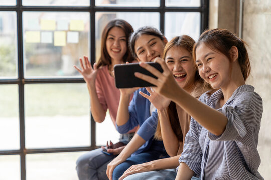Group of beautiful Asian women holding cell phones to take pictures with a group of friends at work. Video call by using FaceTime, Face ID recognition technology, Taking a picture