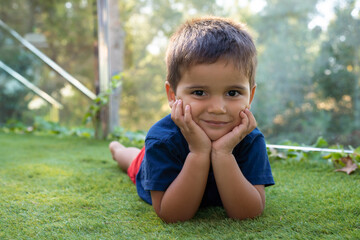 A happy smiling little brunette boy is playing on the green grass.