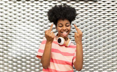 Happy young woman with eyes closed gesturing middle fingers in front of wall