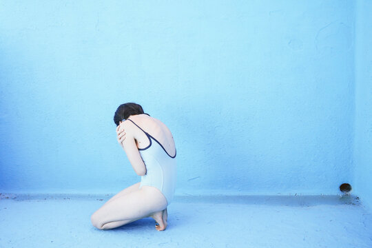 Sad woman sitting in front of blue pool wall