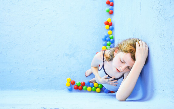 Sad woman standing amidst multi colored balls leaning on blue pool wall