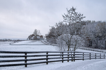 snow covered lane with a fence leading up a hill to a house in the country