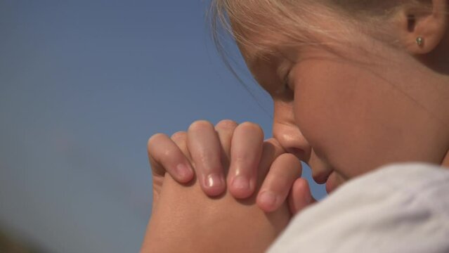 little girl closed her eyes, asks for help, clasped her hands in prayer. The child thanks the Almighty, asks for help. Hands folded in prayer. Close-up of the face, hands of a child in prayer