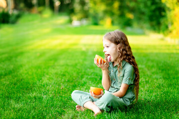 cheerful baby girl in summer on the lawn with oranges on the green grass, having fun and rejoicing, space for text