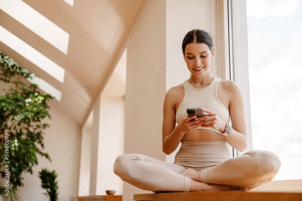 Wall mural young white woman using mobile phone during yoga practice