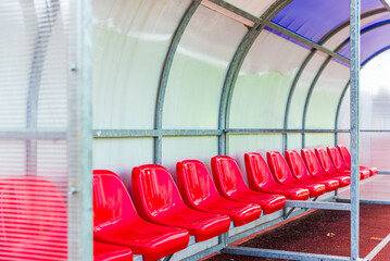 Red bench or seat of staff coach in the stadium of football or soccer in a summer day.