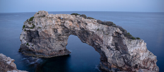 The archway es pontas at Mallorca, Spain in the dawn with some bushes in the foreground.