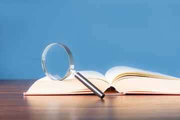 open book with magnifying glass on wooden desk in information library of school or university,...