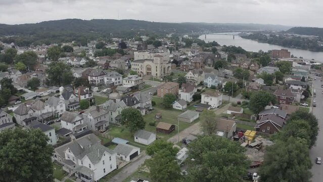 A slow orbiting aerial establishing shot of Rochester, Pennsylvania - a small river town north of Pittsburgh. Bridges over the Ohio River in the distance.  	