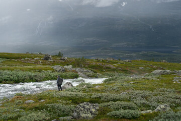 Female hiker with heavy backpack looking for a place to cross wild river in arctic landscape of...
