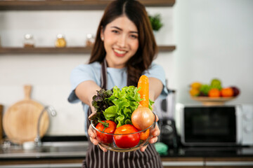 The salad bowl containing of Loose leaf lettuc, Carrot, Tomato and onion in the hand of smile beautiful girl blurr in the back ground.