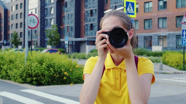 Positive young tourist girl or student photographer takes pictures with a mirrorless camera to create memories. Woman travelling in strange city, smiling, shooting urban landmarks. Front view
