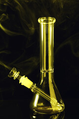 Fototapeta na wymiar Glass bong and smoke on black background, toned in yellow. Smoking device