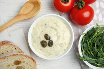 Creamy caper sauce in bowl on white wooden table, flat lay