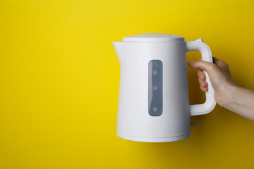 Woman holding modern electric kettle on yellow background, closeup. Space for text