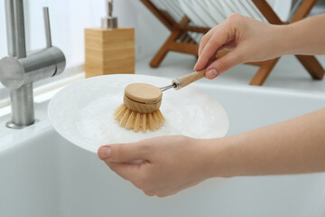 Woman washing plate with brush above sink in kitchen, closeup