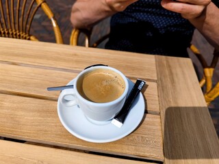 Freshly brewed cup of coffee with a bag of sugar, cup of coffee milk and a spoon on a wooden terrace table. There are no people or trademarks in the shot.