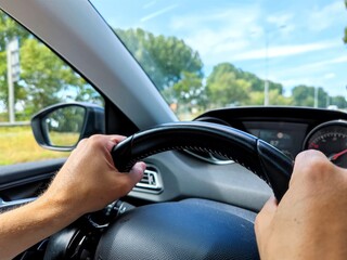 White men hands control a car steering wheel while driving on the road. There are no recognizable persons or trademarks in the shot.