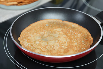 Delicious thin pancake in frying pan on induction stove, closeup