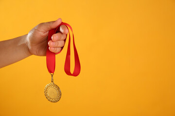 Fototapeta na wymiar Woman holding gold medal on yellow background, closeup. Space for text