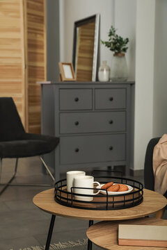 Tray with cups of hot tea and cookies on wooden table in living room. Interior design