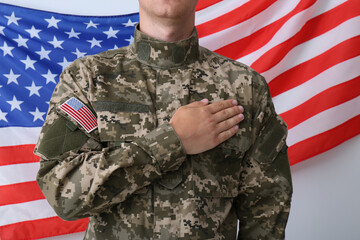 Soldier holding hand on heart near United states of America flag on white background, closeup