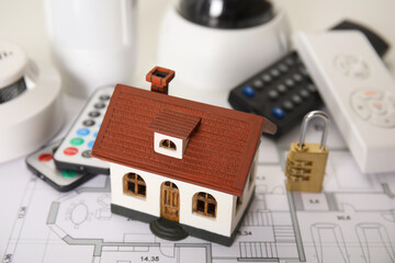House model, CCTV camera, lock, remote controls, smoke and movement detectors on building plan. Home security system