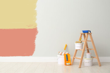 Decorator's kit of tools and paints near white wall with samples of different paints indoors