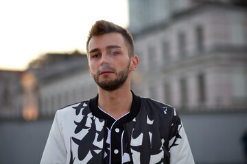 Handsome man in a white and black suit exhales the smoke of a cigarette. A guy with stubble and a...