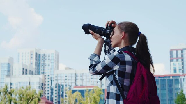 Positive student girl takes pictures of sightseeing attractions while travelling in strange city. Young woman smiling, shooting urban landmarks. Photographer takes pictures to create memories