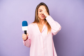 pretty caucasian woman looking shocked, scared or terrified, covering face with hand. journalist...