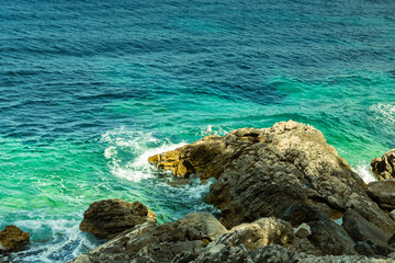 Close-up of a seagull sitting on a rock, rocks sticking out from the sea, sunny day, June, beautiful colors of water from bright green to blue