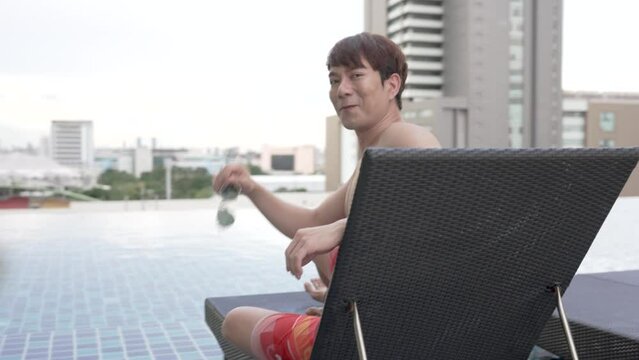 Asian man relax near luxury swimming pool at hotel.