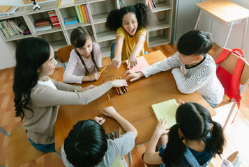 Group of Diverse Elementary School Pupils and Female Asian teacher sitting on chair in circle around learning, discussing new things in classroom. Fun study, education, elementary school concept. - obrazy, fototapety, plakaty