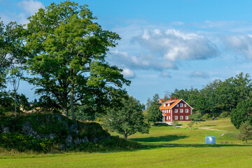 Fototapeta na wymiar Typical red wooden houses in countryside by the sea in nature of southern Sweden on a beautiful sunny summer day. White heystacks in front. Relaxing rural landscape.