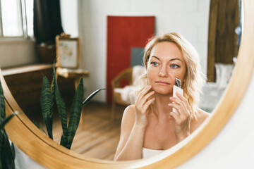A beautiful woman in front of a mirror does an ultrasonic facial cleansing. 
