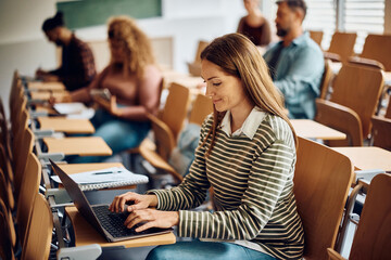 Smiling woman using laptop during lecture at university.