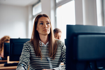 Mid adult female student using desktop PC during computer class in classroom.