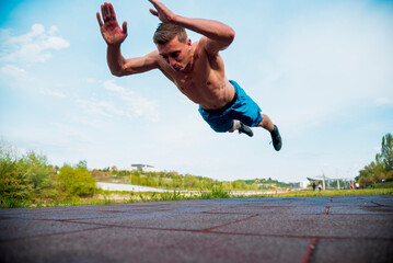 Young shirtless man is exercising outdoor. He is doing clapping push-ups.