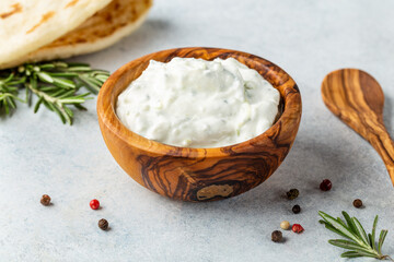 Fototapeta na wymiar Homemade greek tzatziki sauce in an olibe wood bowl bowl on a light stone background. Close-up, horizontal image, copy space