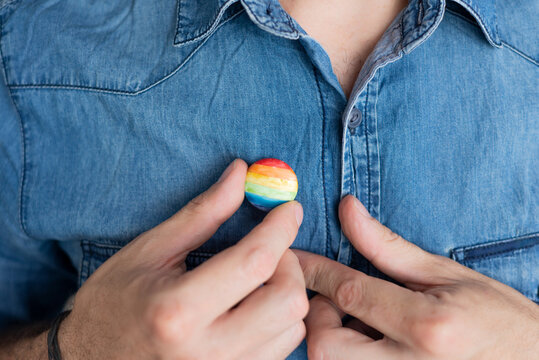 person putting on a multicolored flag badge or pin, symbol of the LGTBIQ collective. pride month. close up shot of man with shirt background
