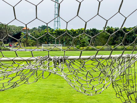 View through ootball gates net to large football field with green lawn, gate opposite and trees. Sports, team sports