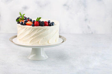 White cake with a wreath made of strawberries and blueberries and raspberries on the white...