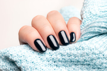 Female hand in blue knitted sweater with beautiful manicure - dark black nails. Nail care concept
