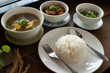 Food set white rice pumpkin soup spicy pork and slice mixed vegetable on wooden table with spoon fork in morning light mood