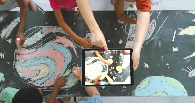 Fun, creative and educational kids drawing activity in a classroom with a teacher taking a photo on a tablet. Children volunteering for a colorful arts project to raise awareness on social media