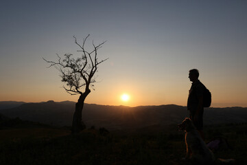 Fototapeta premium silhouette of man and his dog looking sunset from the top of the hill