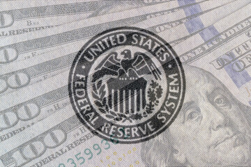Federal Reserve System seal overlay on a bed of hundred dollar bills. The Fed's responsibilities...