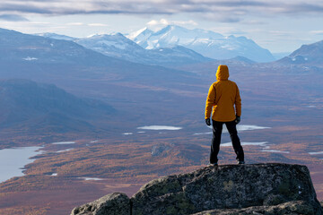 Male hiker overlooking epic view of vast arctic landscape of Stora Sjofallet National Park, Sweden, on autumn day. Mountains and valleys of Lapland. Ahkka massif. View from the top of Lulep Gierkav.