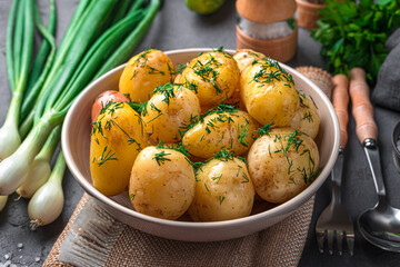 Boiled new potatoes with dill and butter on a dark background. Side view, close-up